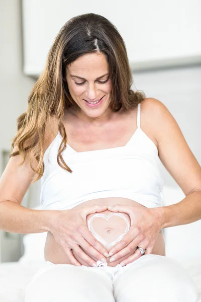 Happy woman with heart on pregnant abdomen