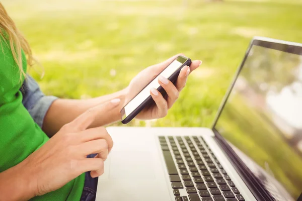 Mid section of woman holding laptop and using smartphone