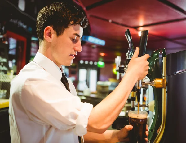 Barkeeper holding beer glass below dispenser tap