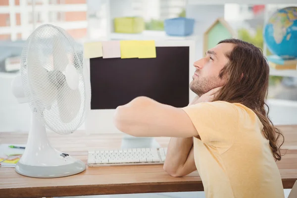 Tired hipster sitting by electric fan on desk