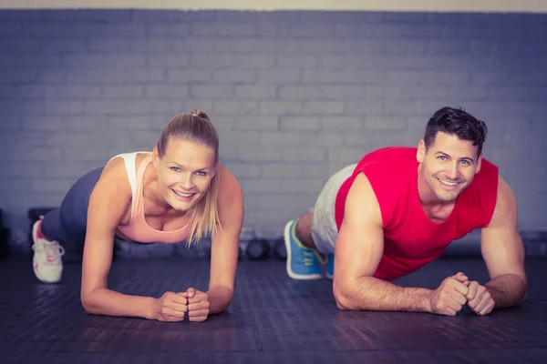 Fit smiling couple planking together in gym