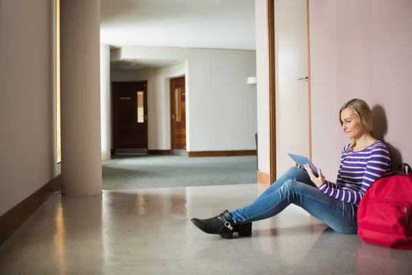 Female student using digital tablet sitting by wall