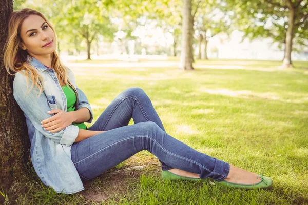 Full length portrait of happy woman sitting under tree