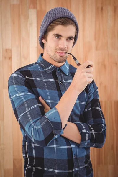Hipster smoking pipe against wooden wall