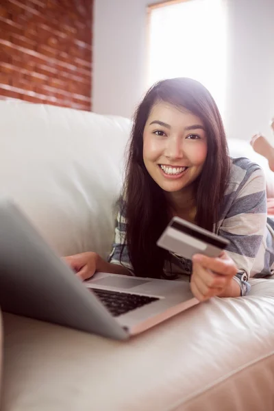 Smiling asian woman on couch using laptop to shop online