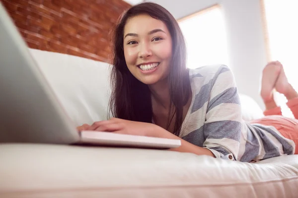 Smiling asian woman on couch using laptop