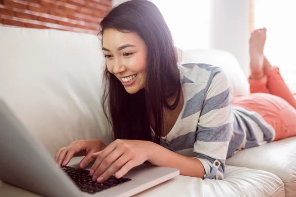 Smiling asian woman on couch using laptop