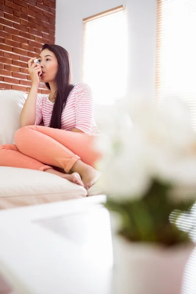 Asian woman using her inhaler on couch