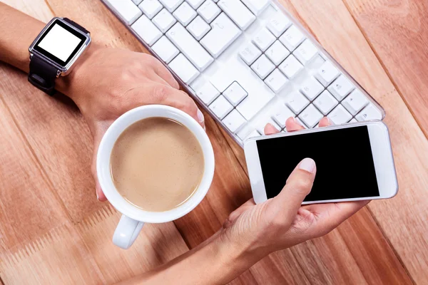 Feminine hands with smartwatch using smartphone and holding hot