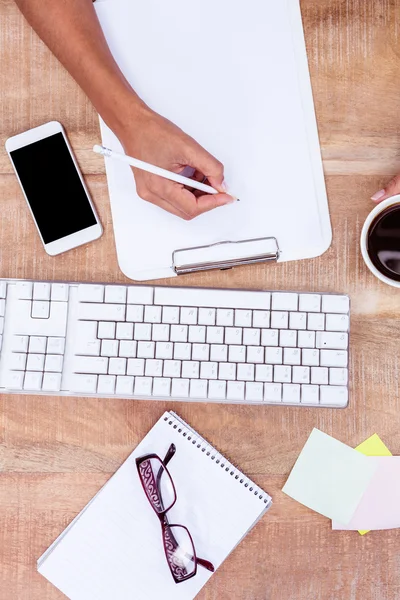 Businesswoman writing on clipboard on desk