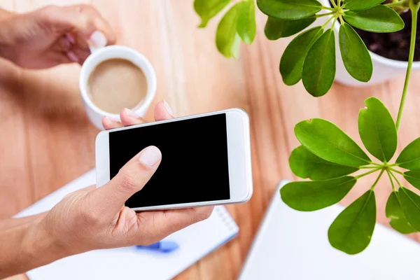 Overhead of feminine hands holding coffee and smartphone