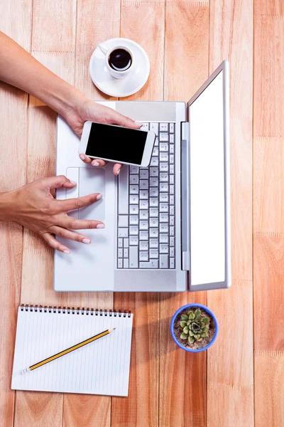 Overhead of feminine hands using smartphone and laptop