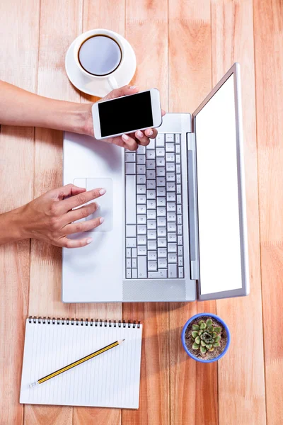 Overhead of feminine hands using laptop and smartphone