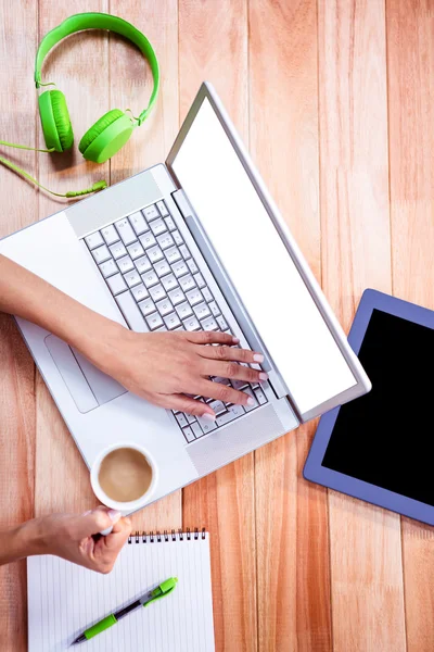 Overhead of feminine hands using laptop and holding coffee