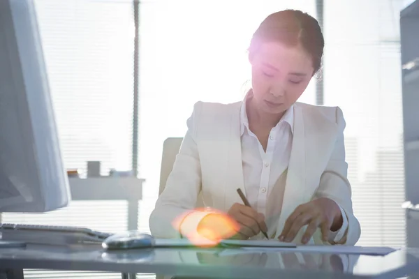 Businesswoman writing on diary on desk