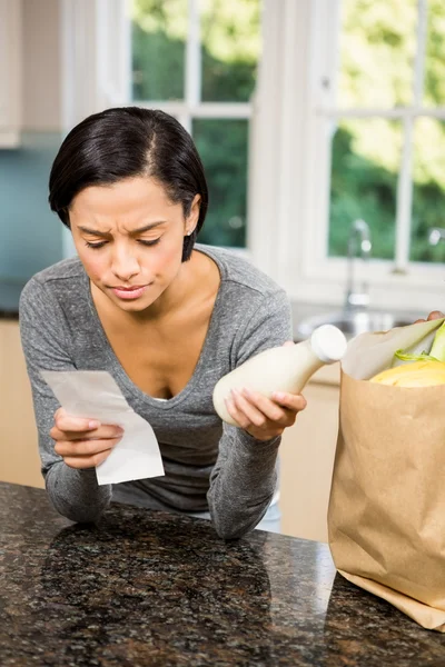 Frowning brunette holding receipt and milk