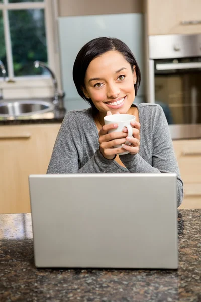 Brunette holding cup while using laptop