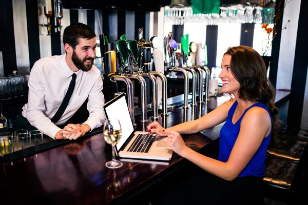 Barman talking to customer using laptop