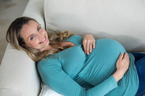 Pregnant woman touching her belly lying on the couch