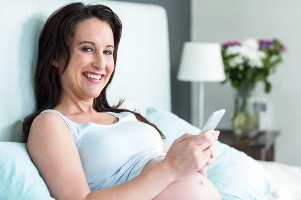 Pregnant woman lying in bed texting