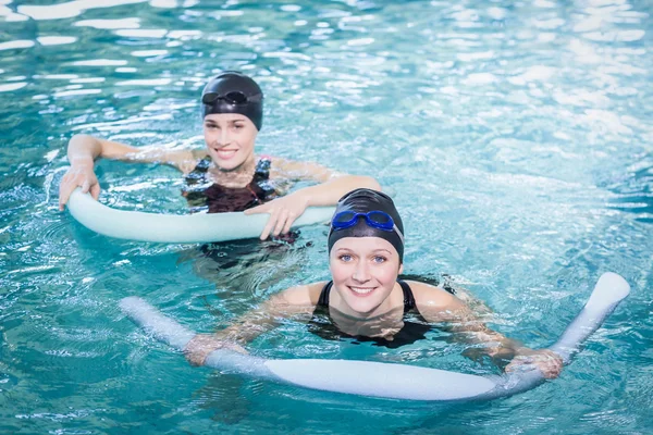 Smiling women in the pool with foam rollers