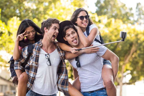 Hip men giving piggy back to their girlfriends and taking selfie