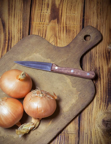 Fresh onion and retro cutting board on old wooden burned table o
