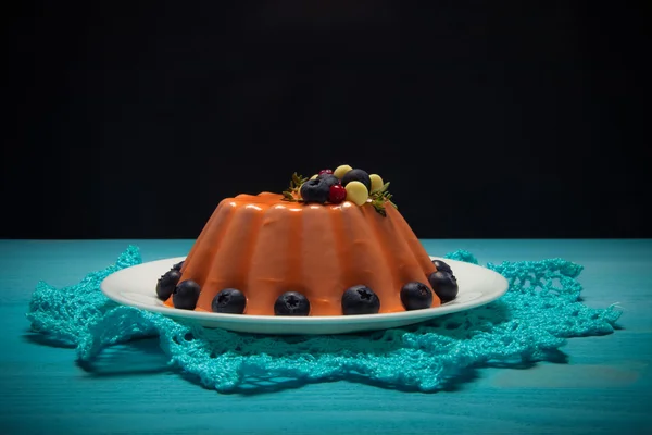 Orange mousse cake with berries n the blue wooden table. Toned