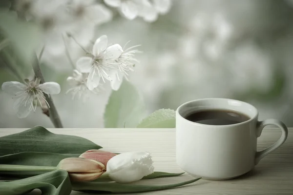 Coffee in a cup and tulips on wooden table opposite a defocused