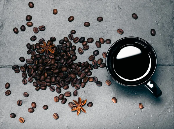 Black cup of coffee and coffee seeds on the slate background. To