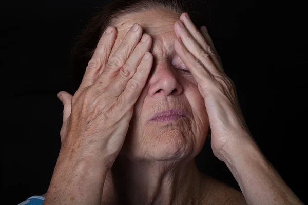 Portrait of elderly woman. Closes eyes with hands