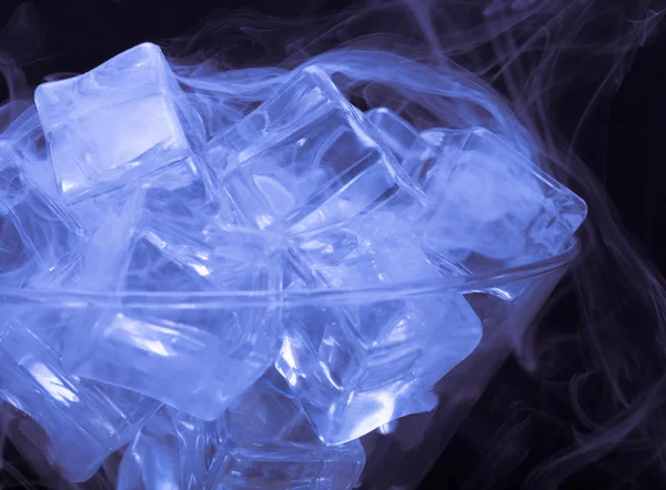 Cloud of smoke over martini glass with ice cubes on black backgr