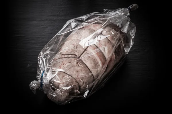 Raw meat with rope in the package on a black background. Toned