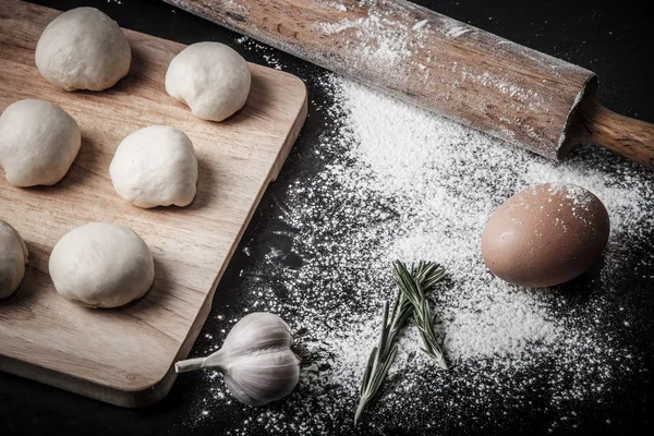 Garlic, rosmary, egg, rolling pin and pieces of dough on the woo