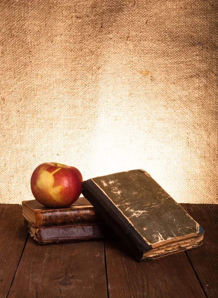 Still life with apple and a stack of old books on old wooden tab
