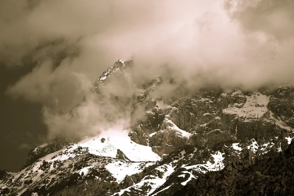 Clouds lie on the snow-covered tops of the rocks. Landscape. Ton