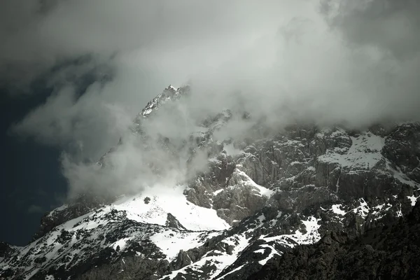 Clouds lie on the snow-covered tops of the rocks. Landscape. Ton