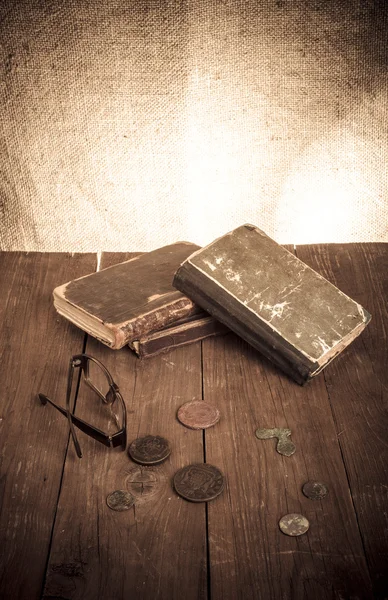 Vintage books and coins and spectacles on old wooden table. Tone