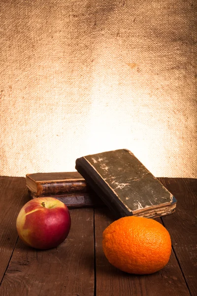 Old books, apple and orange lying on an old wooden table