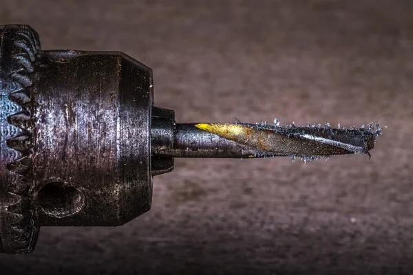 Drill with a drill bit and metal shavings on a blurred backgroun