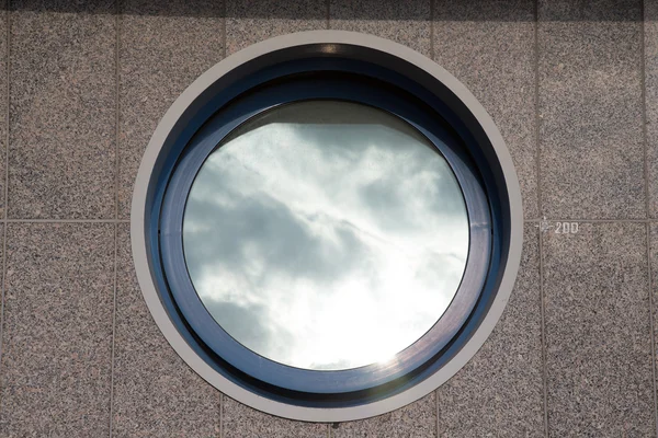 Ajar round window on the tiled granite wall - part of the urban