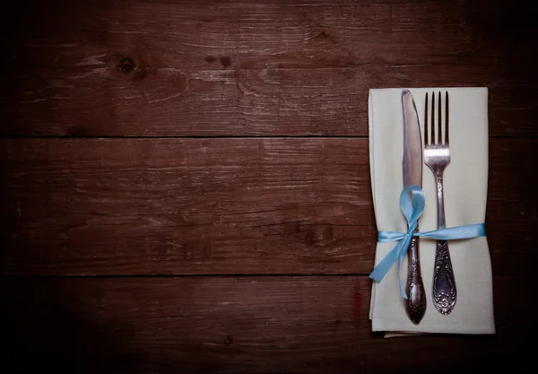 Fork and knife in napkin on wooden background. Toned