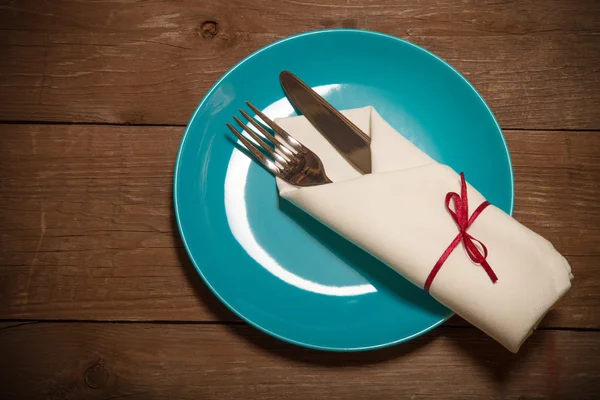 Plate, fork and knife in napkin on wooden background. Toned