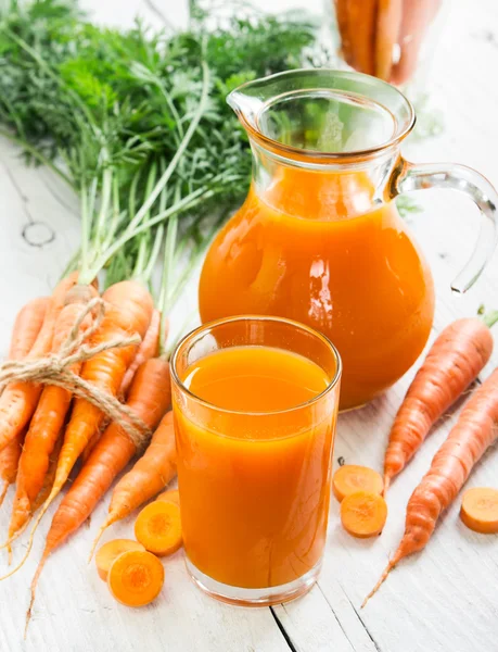 Carrot juice in glass and jug and fresh carrots