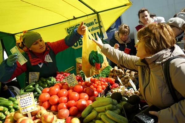 MOSCOW, RUSSIA - OCTOBER 04, 2015: Traditional Food Fair on the weekend. Vegetable stall, seller transfers to a customer with shopping bag.