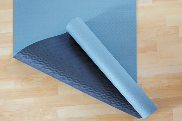Thick anti slip blue and black fitness yoga practice or meditation mat on wooden floor
