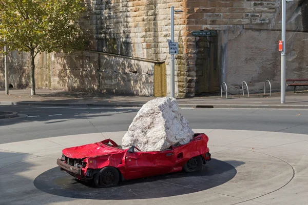 Huge stone dropped on red car as outdoor sculpture at Pottinger Street, Sydney