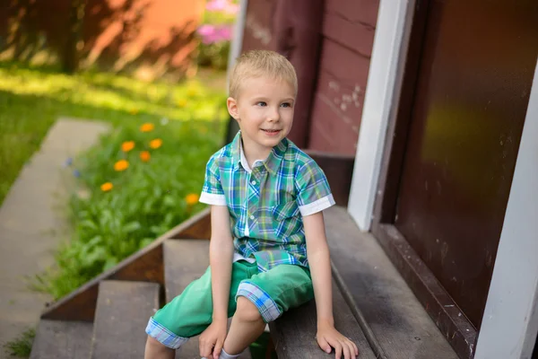 Smiling young blond boy sitting on porch steps at home