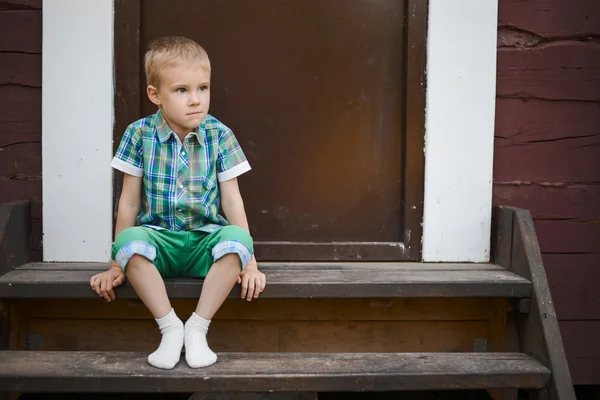 Smiling young blond boy sitting on porch steps at home
