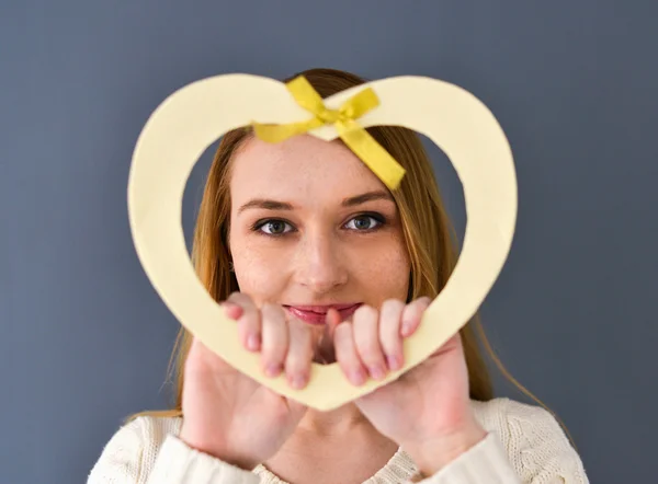 Closeup portrait of young female holding heart shape isolated on gray background